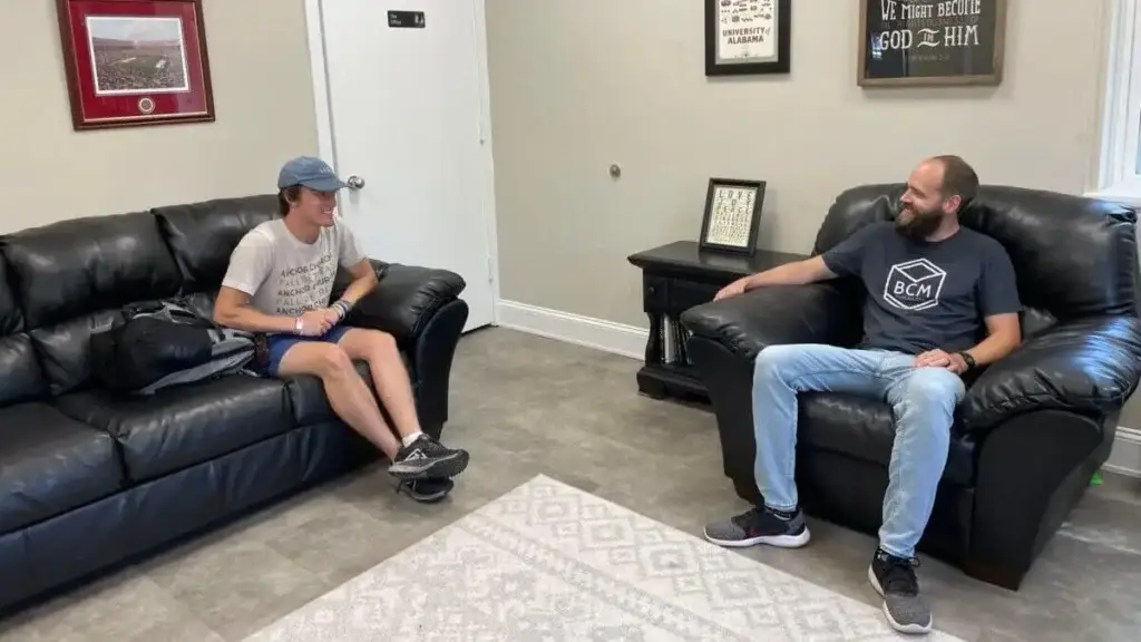 College student sits on couch talking with his ministry mentor seated in a large chair