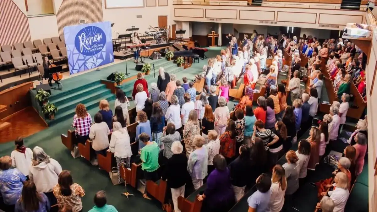 View of people standing in pews facing stage during Renew Conference