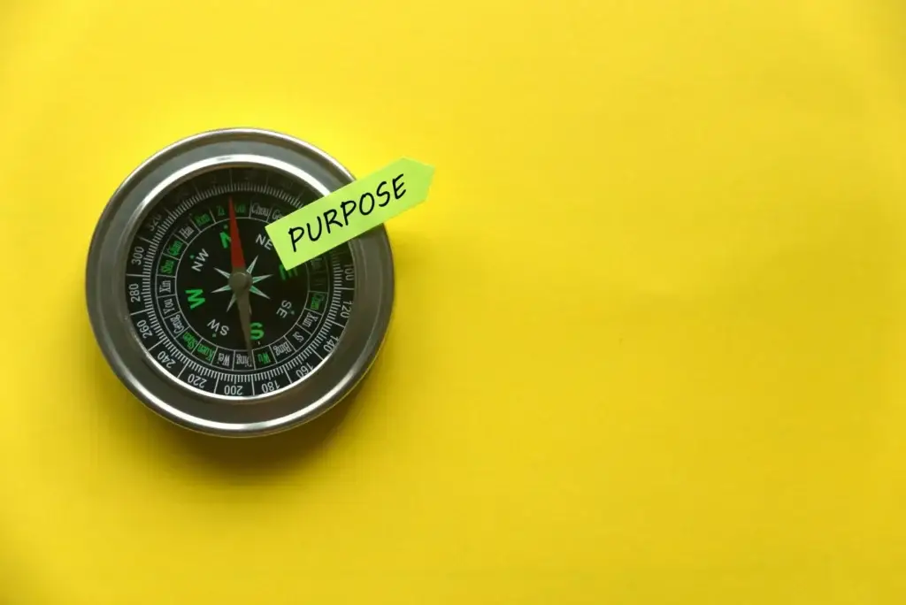 Top view of a compass and sticky note written with "Purpose" on yellow background