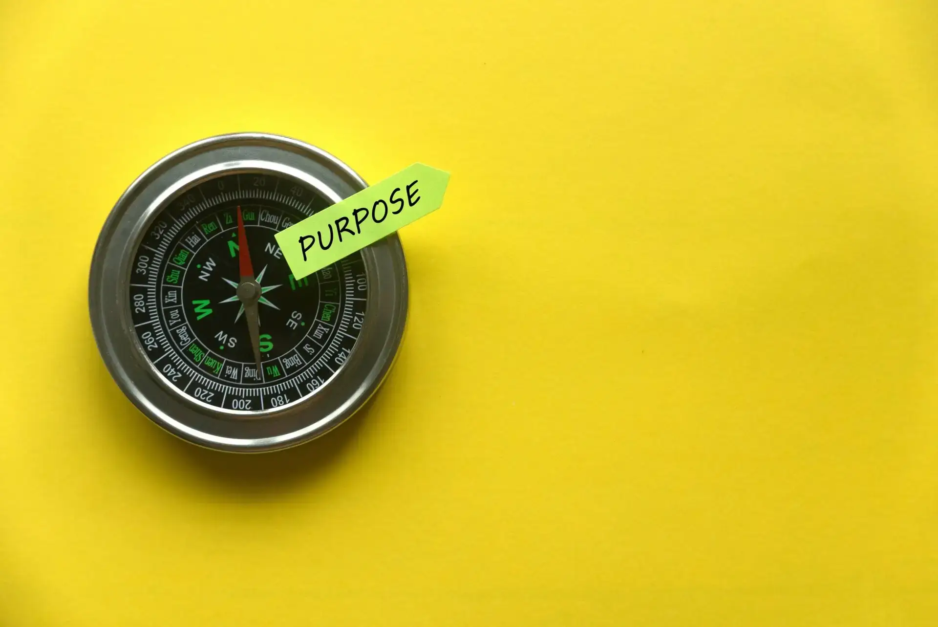 Top view of a compass and sticky note written with "Purpose" on yellow background