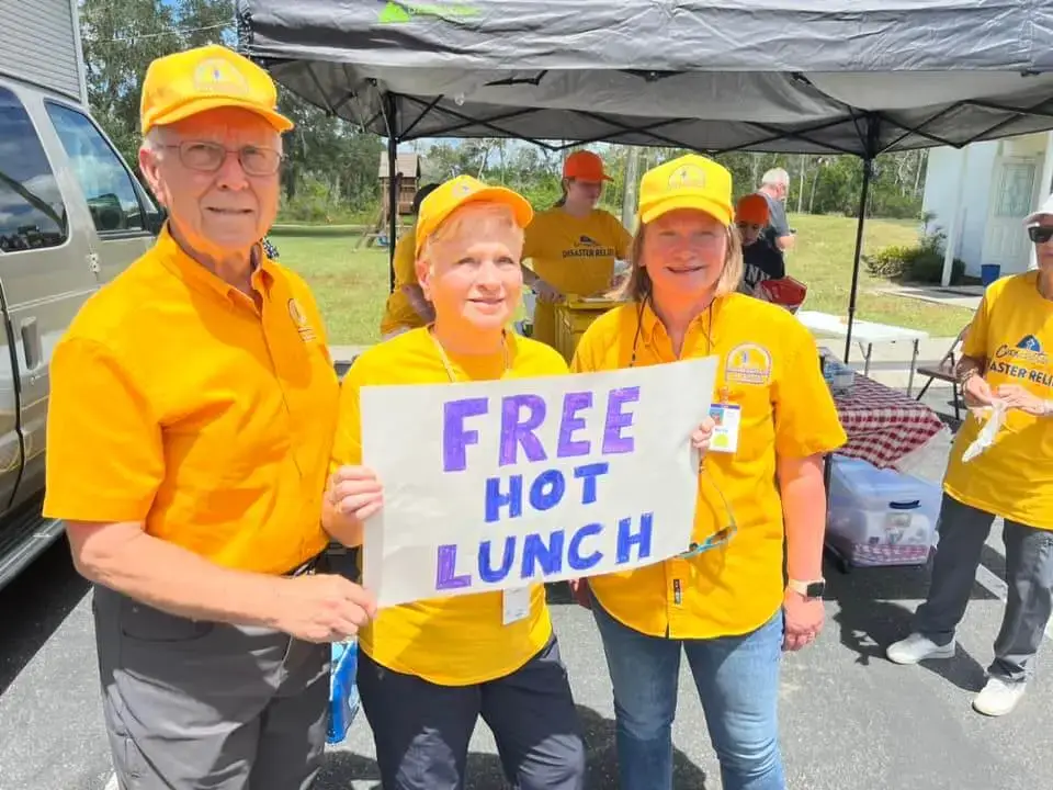 Disaster Relief Volunteers holding up a sign saying, "Free Hot Lunch".