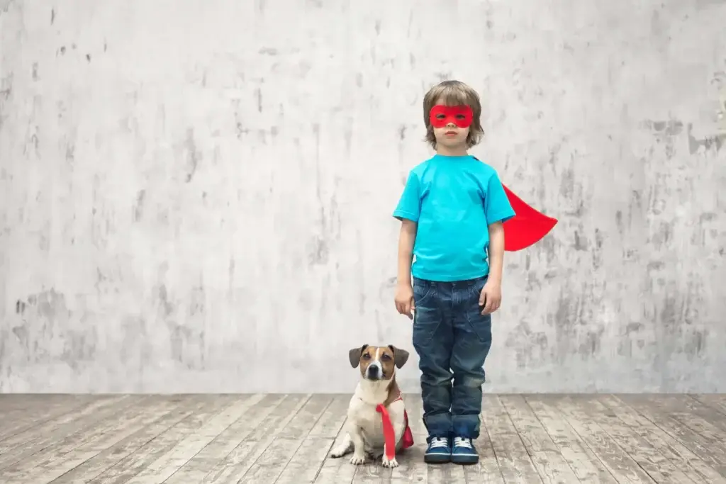 Little boy in super hero cape and mask with dog beside him also wearing a cape