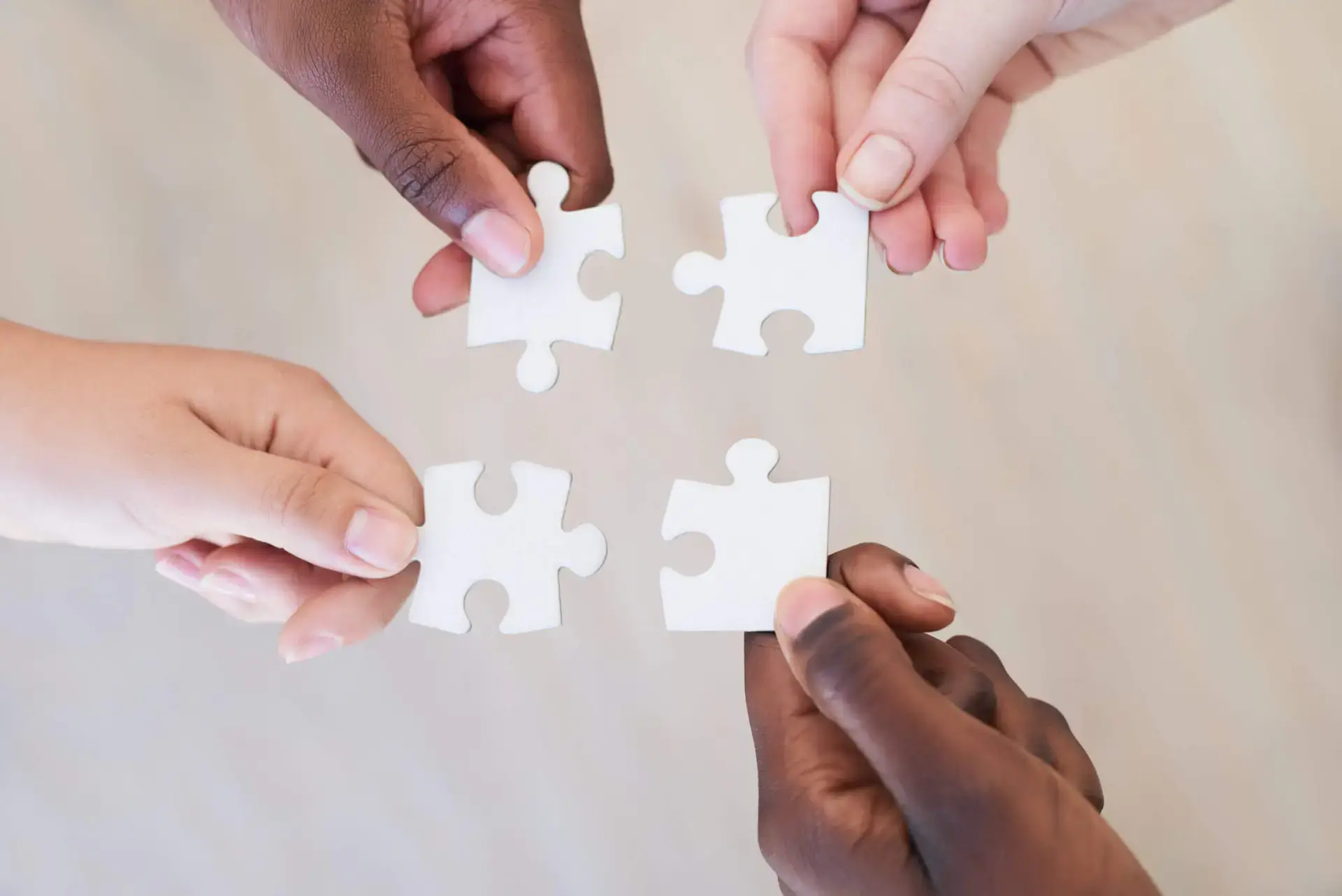 Four different hands each holding a white puzzle piece that are able to connect together