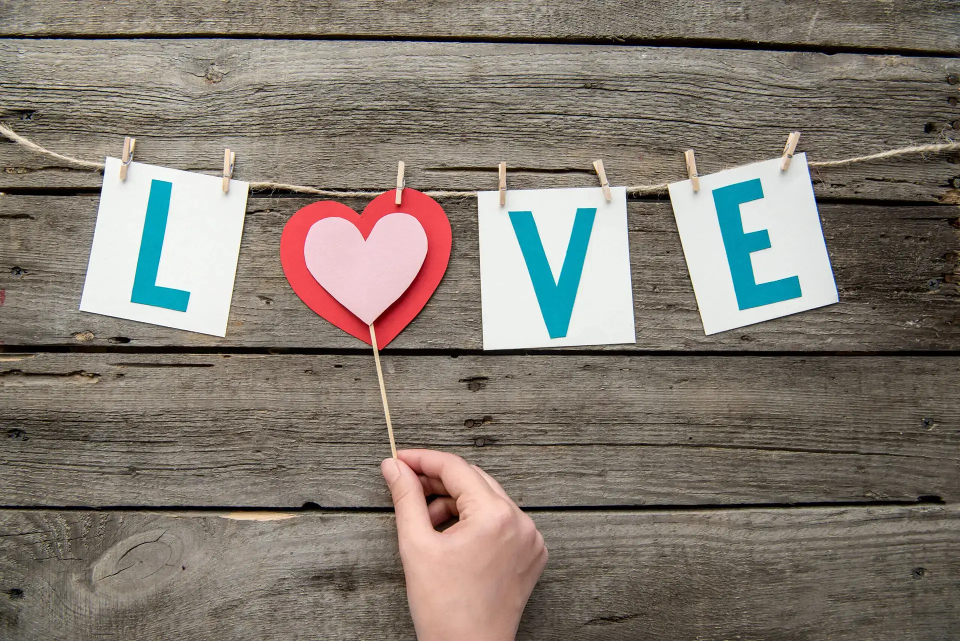 Handmade party decoration with love sign and human hand holding heart on wooden table