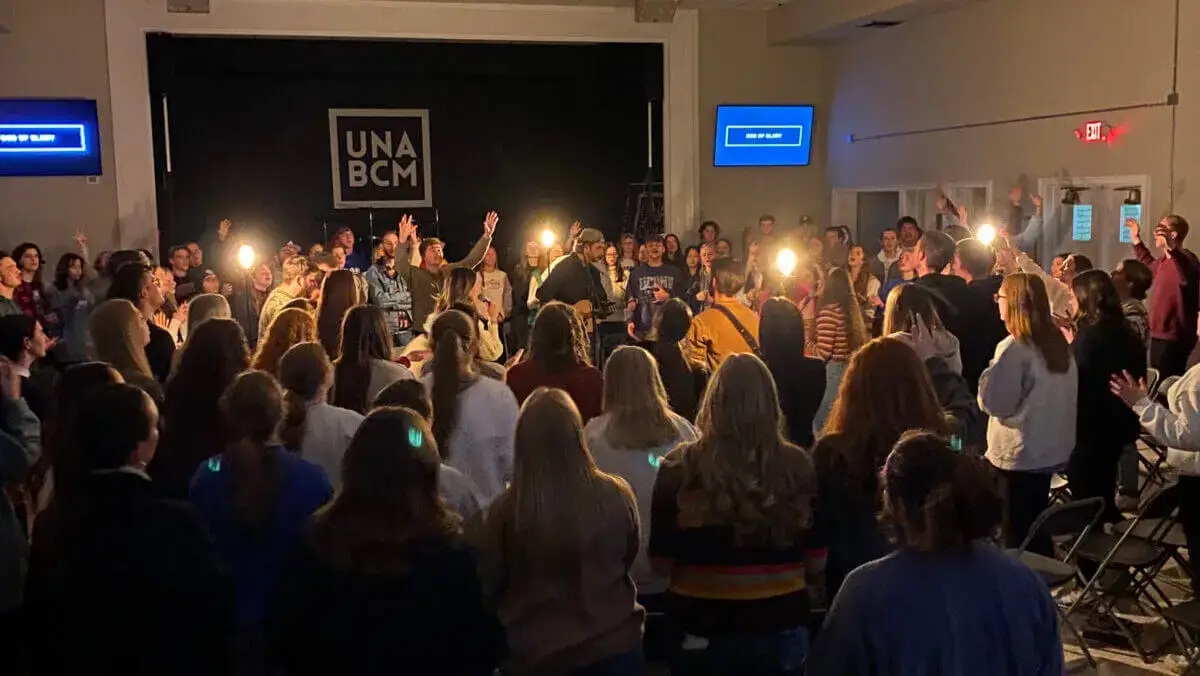 A large group of college students gather around a praise band for a time of worship on campus