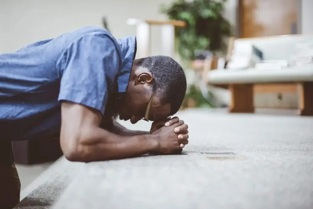 Man praying on his knees with his head bowed at church