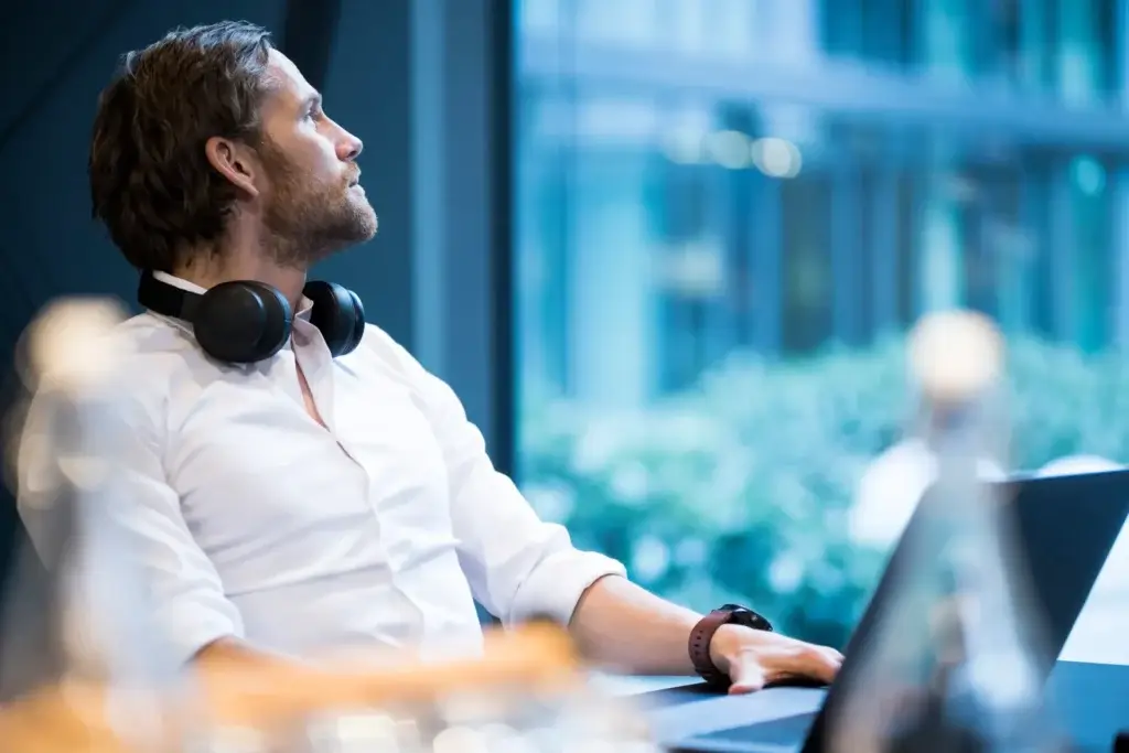 Man working on a laptop looking out of a window daydreaming