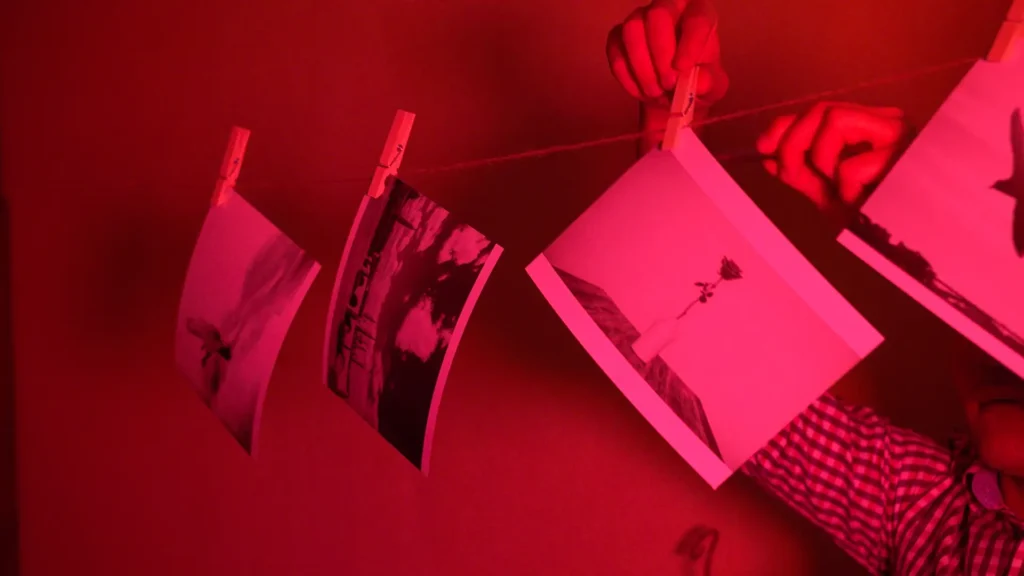 Hands hanging up a photo to dry in a dark room. Red hue across entire image.