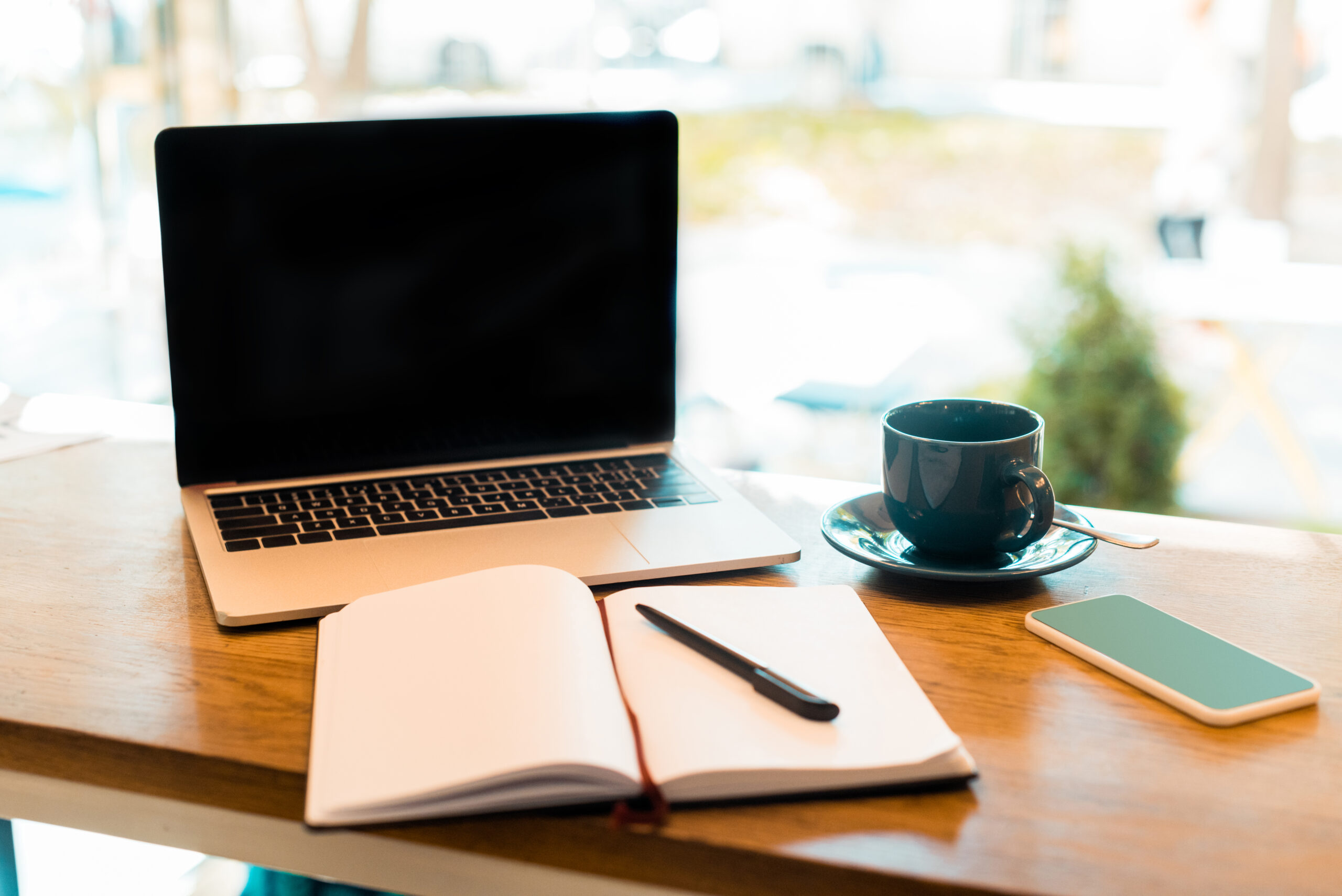 laptop with blank screen, notebook and cup of tea on wooden cafe counter